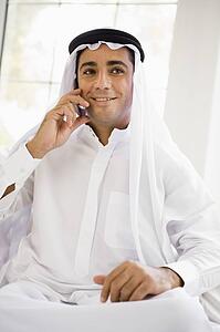 Man sitting indoors on cellular phone smiling (high key)