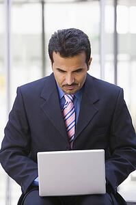Businessman sitting outdoors by building with a laptop (high key/selective focus)