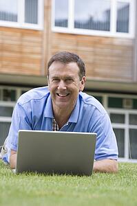 Man lying on lawn of school with laptop