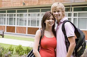 Two students standing outdoors with arms around waists smiling