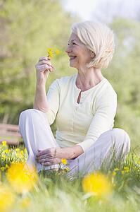 Woman sitting outdoors smiling and holding a Buttercup flower