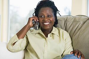 Woman sitting in living room using telephone and smiling