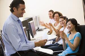 Man with clipboard giving lecture in applauding computer class