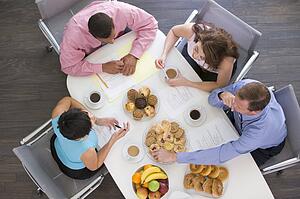 Four businesspeople at boardroom table with breakfast