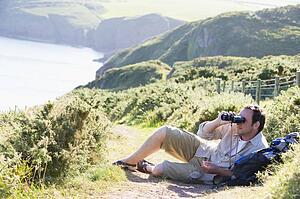 Man relaxing on cliffside path using binoculars
