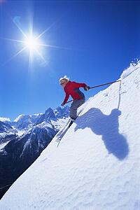 Skier coming down snowy hill smiling (lens flare)