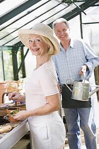 Woman in greenhouse planting seeds and man holding watering can smiling
