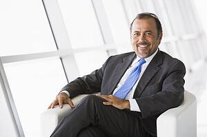 Businessman sitting indoors smiling (high key/selective focus)