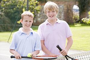 Two young male friends with rackets on tennis court smiling