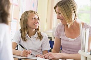 Student in class taking notes with teacher helping