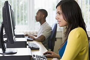 Woman sitting at a computer terminal with man in background (selective focus/high key)