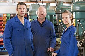 Three machinists in workspace by machine talking