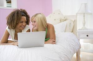 Teenage Girls Lying On Bed Using Laptop 
