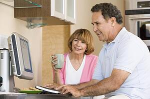 Couple in kitchen with computer and coffee smiling