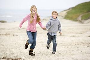 Two young children running on beach holding hands smiling