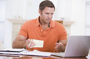 Man in dining room with laptop holding paperwork