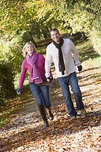Couple outdoors running on path in park holding hands smiling (selective focus)