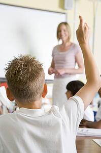 Student volunteering in class with teacher at board (selective focus)
