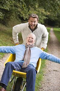 Son pushing senior father in wheelbarrow