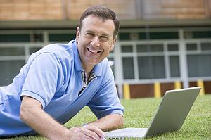 Man lying on lawn of school with laptop