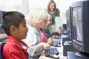 Four children at computer terminals with teacher in background (depth of field/high key)