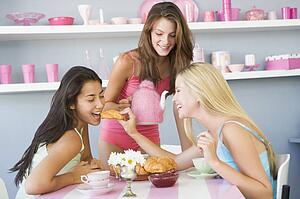 Three young woman sitting at a table having tea and a snack