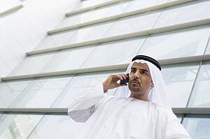 Businessman standing outdoors by building on cellular phone (selective focus)