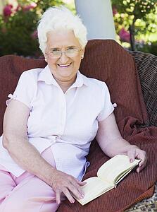 Senior woman sitting outdoors on a chair reading a book