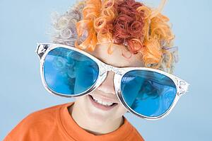 Young boy wearing clown wig and sunglasses smiling