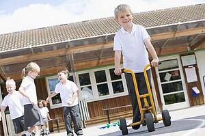 Students playing outdoors during recess one with a tricycle scooter (selective focus)