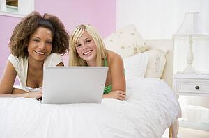 Teenage Girls Lying On Bed Using Laptop 
