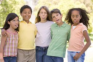 Five young friends standing outdoors making funny faces