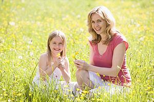 Mother and daughter outdoors holding flower smiling