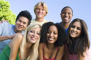 Six people outdoors huddling over camera