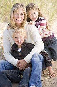 Mother and two young children sitting on beach smiling