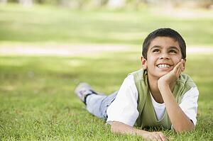 Young boy outdoors lying in grass and smiling (selective focus)