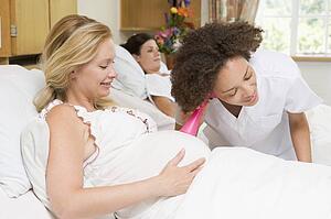Nurse checking pregnant woman's belly and smiling