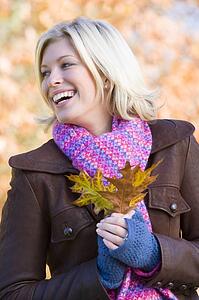 Woman outdoors in park holding leaf smiling (selective focus)