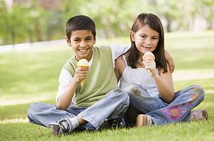Two young children outdoors in park with ice cream smiling (selective focus)