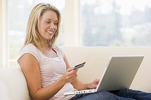 Woman in living room using laptop and holding credit card smiling