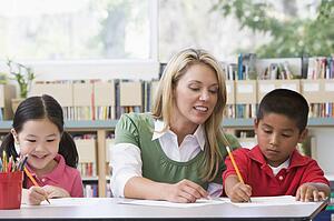 Two students in class writing with teacher helping