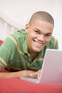 Teenage Boy Lying On Bed Using Laptop 