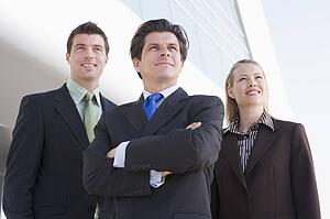 Three businesspeople standing outdoors by building smiling