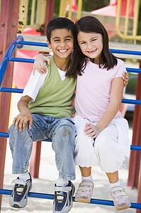 Two young children sitting on playground structure smiling (selective focus)