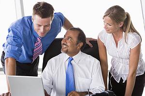 Three businesspeople in office with laptop talking and smiling (high key/selective focus)