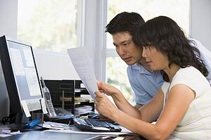 Couple in home office with computer and paperwork pointing