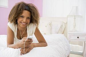 Teenage Girl Lying On Bed Using Mp3 Player