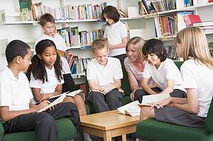 Seven students in library reading books with teacher