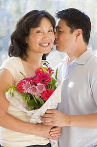 Husband and wife holding flowers kissing and smiling