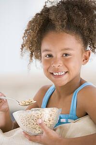 Young girl eating cereal in living room smiling